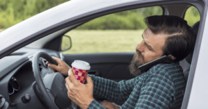 A man speaking on phone and drinking coffee while driving his car